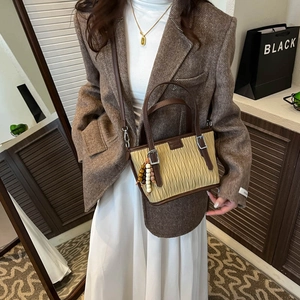 Detail of beige pleated bucket bag with brown handles and stylish beaded charm accessory