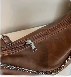 Detail of retro brown shoulder bag featuring a smooth zipper and silver woven chain strap