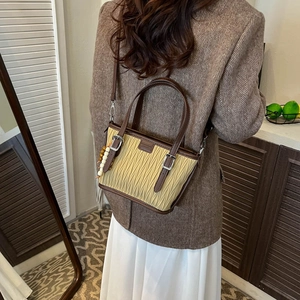 Detail of pleated tote bag with bead pendant and leather strap worn by a model