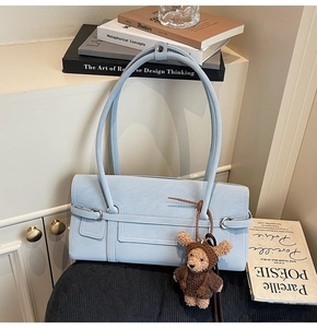 Detail of light blue faux leather baguette bag with metal buckle and cute bear charm