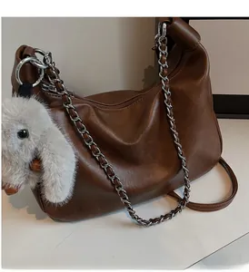 Detail view of vintage brown leather bag featuring a chunky silver chain and plush bunny charm