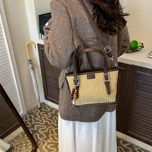 Detail view of a beige pleated bucket bag with brown leather trim and wooden bead charm