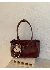 Dettaglio della borsa a tracolla rosso scuro in pelle testurizzata e ciondolo peluche