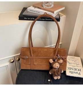 Detail of brown suede shoulder bag with visible stitching and plush bear charm