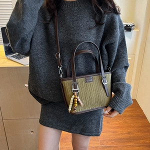 Detail of olive green pleated bucket bag with brown leather handles and wooden bead charm