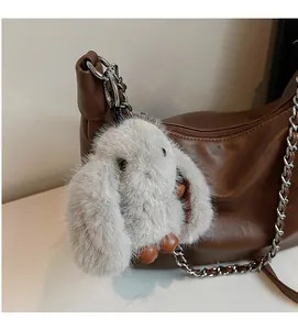 Detail of gray plush rabbit charm with leather accents on a brown crossbody bag
