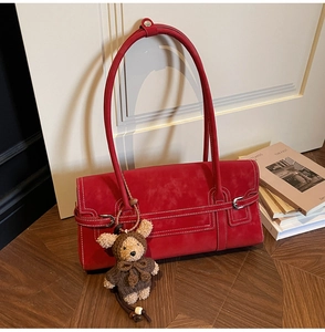 Detail of red suede baguette bag with contrast stitching and teddy bear charm accessory
