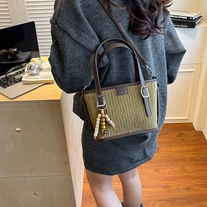Detail view of olive green pleated bucket bag with brown leather handles and wooden beads
