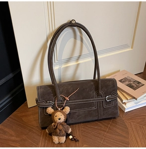 Detail of dark brown faux suede shoulder bag with contrast stitching and bear charm