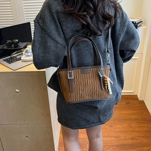 Brown bucket bag with Matelassé pleats and beaded charm shown in a lifestyle setting