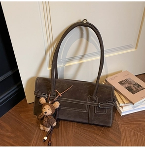 Close-up of retro brown faux suede shoulder bag with white stitching and bear charm