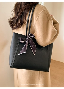 Detail of black pebbled leather tote bag with polka dot scarf on a camel coat