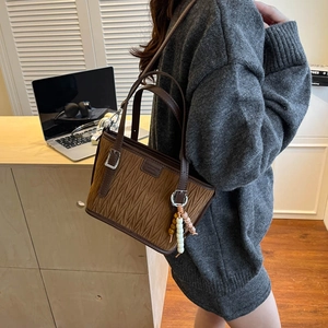 Brown pleated leather tote bag with round bead charm on a wooden desk background