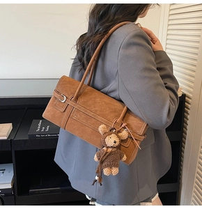 Close-up of caramel leather tote bag with side buckle and cute teddy bear charm