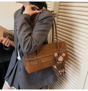 Detail of brown suede tote bag with decorative strap and plush bear charm on model