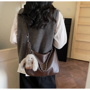 Detail of deep brown crescent shoulder bag with silver chain and plush bunny charm