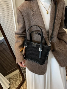 Retro black bucket bag with pleated texture and ethnic charm pendant worn by a model