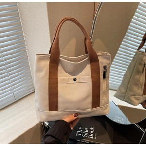 Detail of canvas tote bag showing brown braided handles and side metal zipper pocket