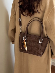 Deep brown pleated bucket bag with beaded charm shown on an elegant wool coat