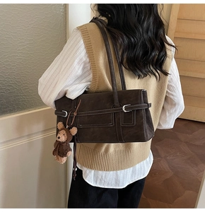 Detail of dark brown tote bag with white contrast stitching and a cute teddy bear charm