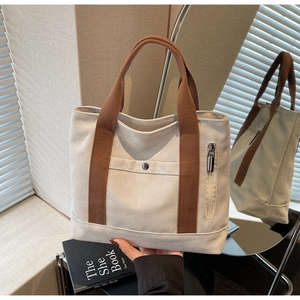 Detailed close-up of a canvas tote bag with brown handles and a functional metal snap pocket