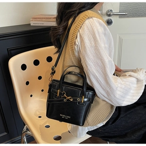 Detail of black leather bucket bag with gold metal hook clasp and brand logo lettering