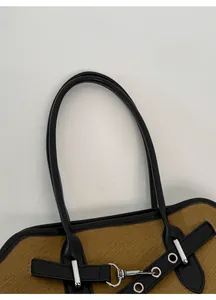 Close-up of brown textured fabric tote with black leather trim and silver metal buckle