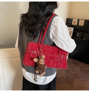 Detail of red leather shoulder bag with white stitching and cute plush bear charm