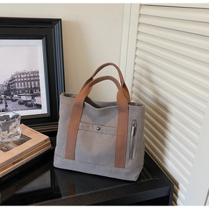 Detail view of a grey canvas tote bag with brown straps and functional zip pocket