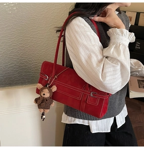 Detail of red vintage shoulder bag with white stitching and plush bear charm