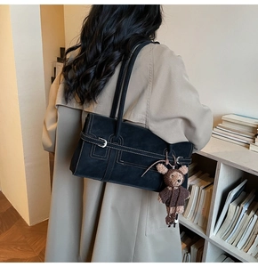 Detail of black suede shoulder bag with white contrast stitching and a cute bear charm