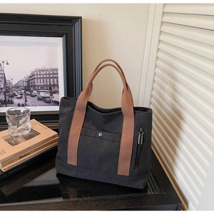 Detail of black canvas tote bag with brown woven handles and metal snap pocket detail