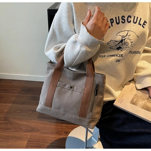 Detail of grey canvas tote bag with brown handles and functional front utility pockets