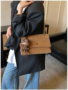 Close-up of brown suede crossbody bag with gold chain and cute plush cat pendant