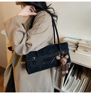 Detail of black matte shoulder bag with white stitching and cute teddy bear pendant