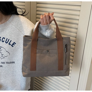 Detail of grey canvas tote bag with brown leather straps and multi-pocket design