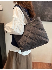 Deep grey quilted nylon tote bag with rhombus stitching shown on model in a cozy indoor setting