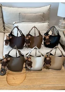 Six colors of textured leather bucket bags with teddy bear charms on a wooden table
