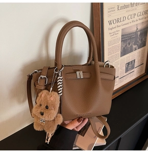 Détail du sac seau en cuir marron avec boucle en métal et breloque chiot en peluche