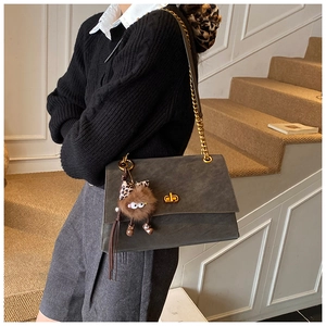 Close-up of charcoal gray suede shoulder bag with gold chain strap and cute monster charm