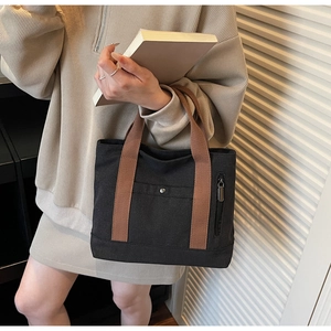 Close-up of black canvas tote bag featuring brown woven handles and metal snap pockets
