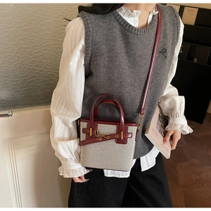 Detailed view of a vintage beige canvas bucket bag with burgundy leather trim and gold buckle