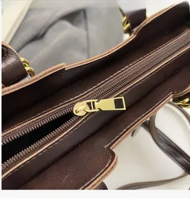 Detailed close-up of smooth gold metal zipper and textured dark brown leather on crossbody bag