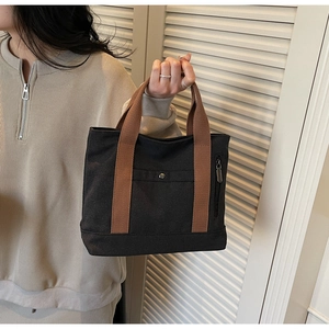 Detail view of canvas tote bag with brown straps, side zipper and front snap button pocket