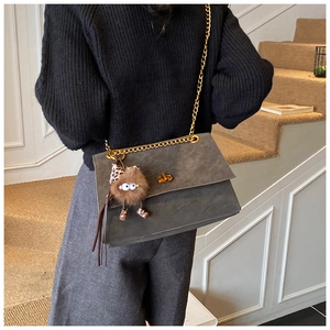 Detail of grey chain crossbody bag with golden turn-lock and fuzzy monster charm