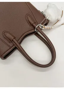 Detail of brown lychee grain leather bucket bag with plush charm and reinforced handle