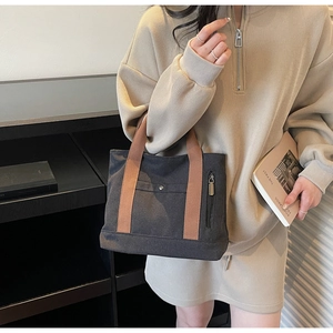 Detail of canvas tote bag featuring brown straps, a front pocket, and side zipper design