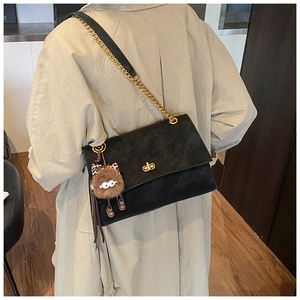 Detail of black leather shoulder bag with gold twist lock and plush monster charm pendant