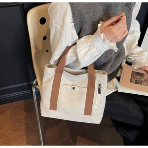 Detail of a beige canvas tote bag featuring brown handles and functional side zipper pocket