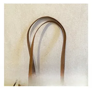 Detail of slim brown leather handles with contrast white stitching on a tote bag